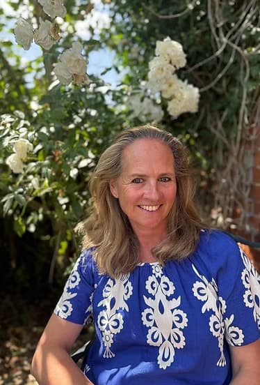 Sheelagh Chetwode sitting in a garden in front of white roses, smiling