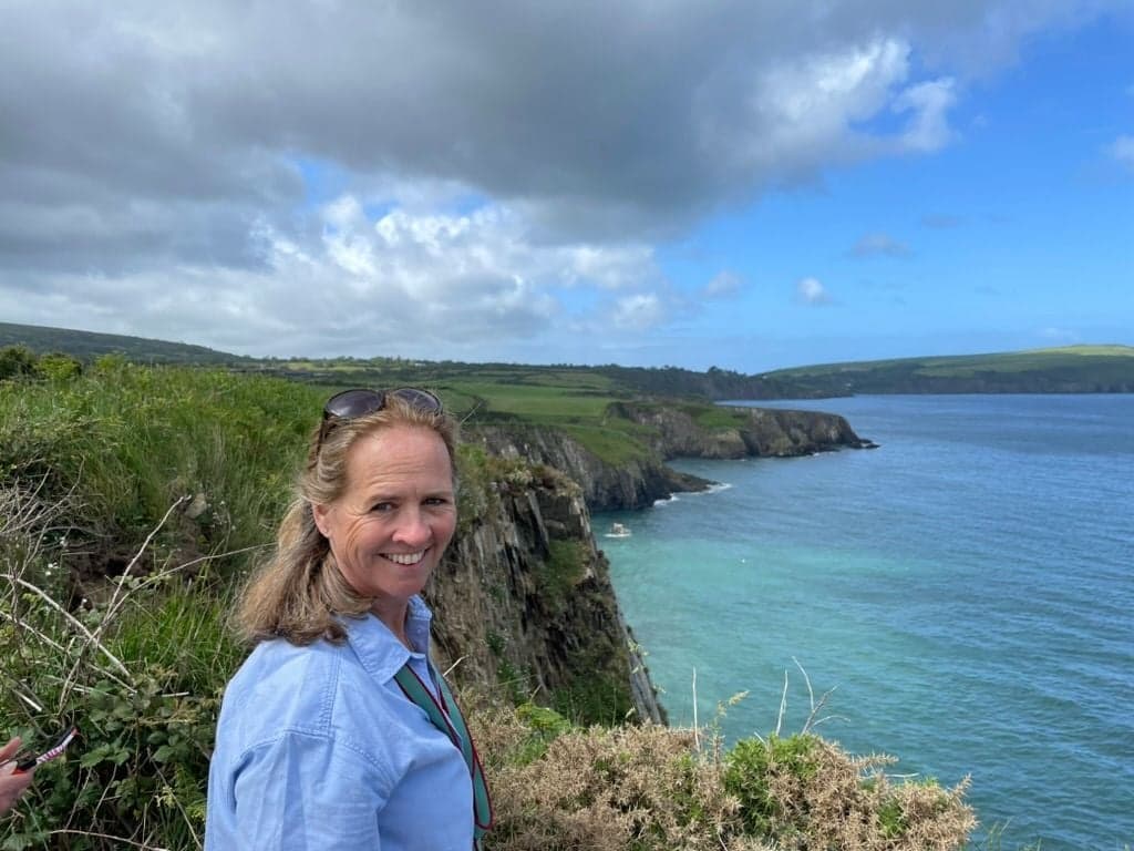 Sheelagh Chetwode on a coastal path, with cliffs and the sea behind her
